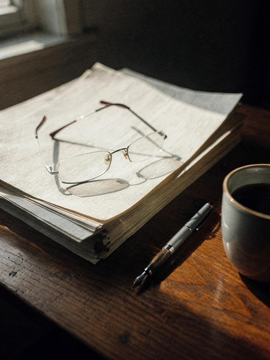Reading glasses and a fountain pen resting on a stack of documents in late afternoon light